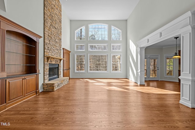 unfurnished living room featuring a stone fireplace, a high ceiling, light wood-style floors, and ornate columns