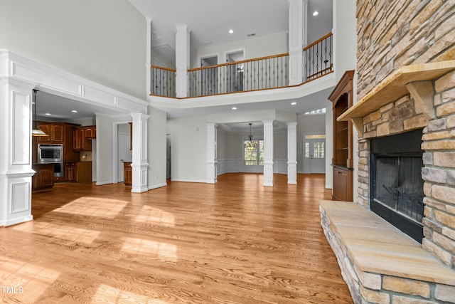 unfurnished living room featuring a decorative wall, light wood-style floors, a fireplace, and ornate columns