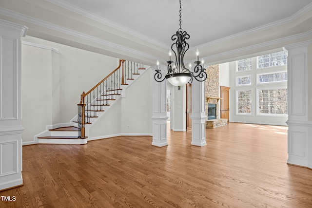 unfurnished dining area with decorative columns, a fireplace, stairs, crown molding, and light wood-type flooring