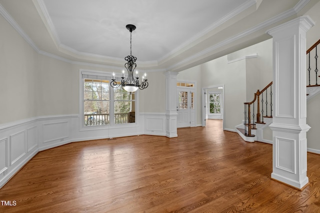 interior space featuring wood finished floors, decorative columns, ornamental molding, stairs, and a chandelier