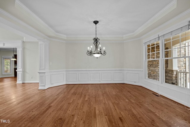 unfurnished dining area featuring visible vents, wainscoting, wood finished floors, a notable chandelier, and ornate columns