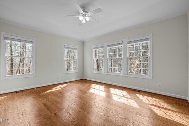 unfurnished room with ceiling fan, wood finished floors, visible vents, and baseboards