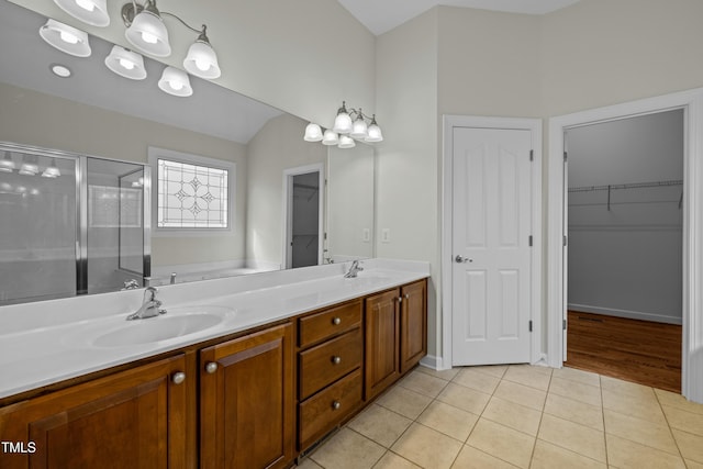 full bath with double vanity, a sink, a shower stall, a spacious closet, and tile patterned floors