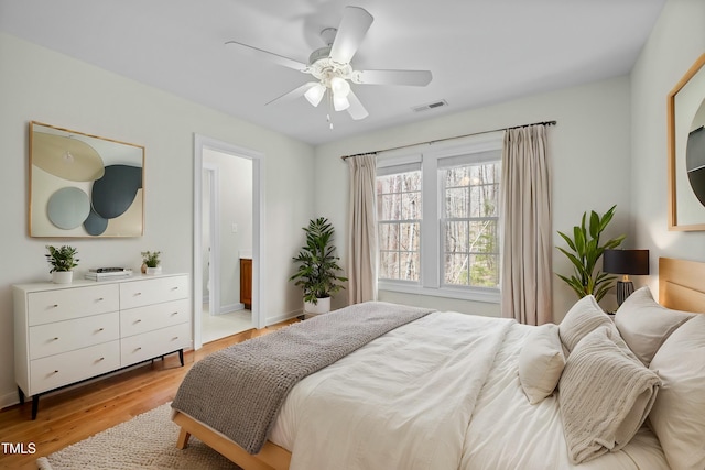 bedroom featuring light wood-style flooring, a ceiling fan, visible vents, and connected bathroom