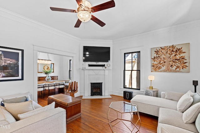 living area with wood-type flooring, crown molding, and a fireplace with flush hearth