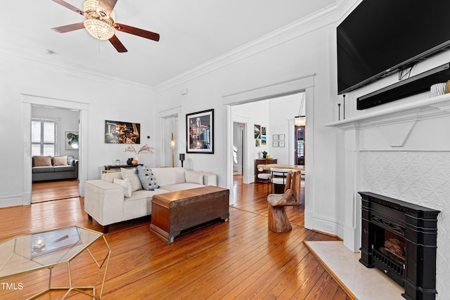 living area with hardwood / wood-style flooring, crown molding, ceiling fan, and a tiled fireplace