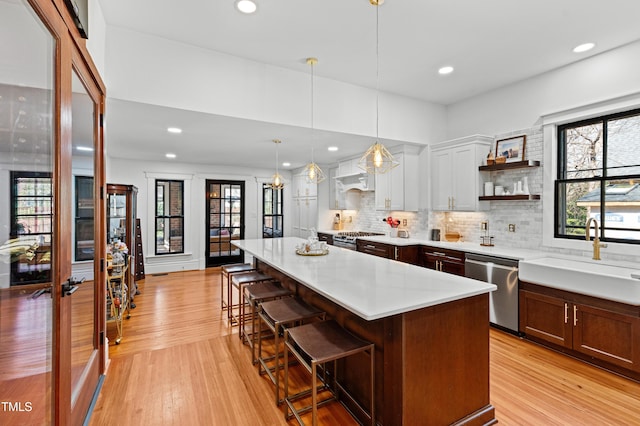 kitchen with light wood finished floors, a kitchen breakfast bar, stainless steel appliances, light countertops, and a sink