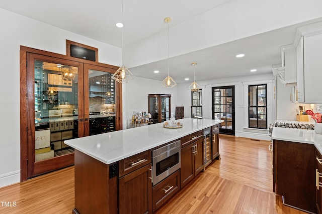 kitchen featuring pendant lighting, stainless steel microwave, light wood-style floors, white cabinetry, and a kitchen island