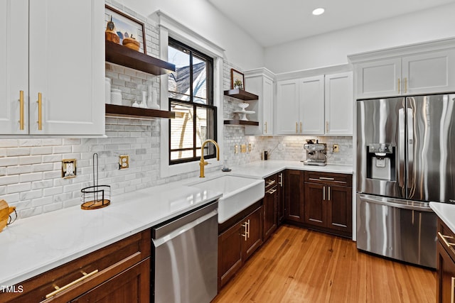 kitchen with a sink, stainless steel appliances, light wood-style floors, open shelves, and backsplash