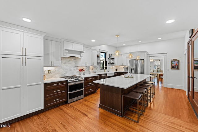 kitchen featuring stainless steel appliances, a breakfast bar, light countertops, light wood finished floors, and tasteful backsplash