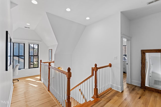 corridor with visible vents, light wood finished floors, vaulted ceiling, and an upstairs landing