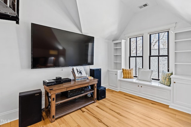 living room featuring light wood finished floors, visible vents, and vaulted ceiling