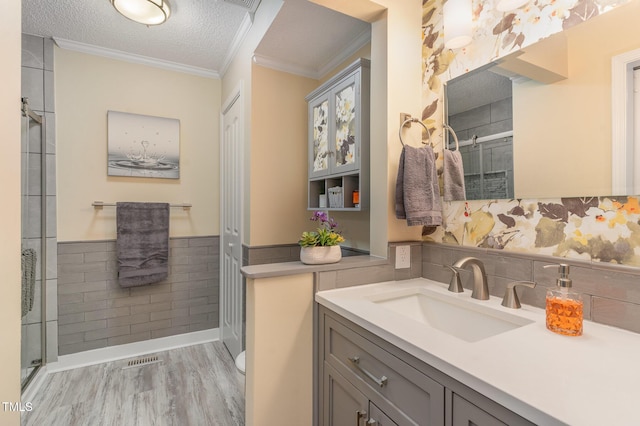 bathroom featuring crown molding, a shower with door, hardwood / wood-style floors, vanity, and a textured ceiling