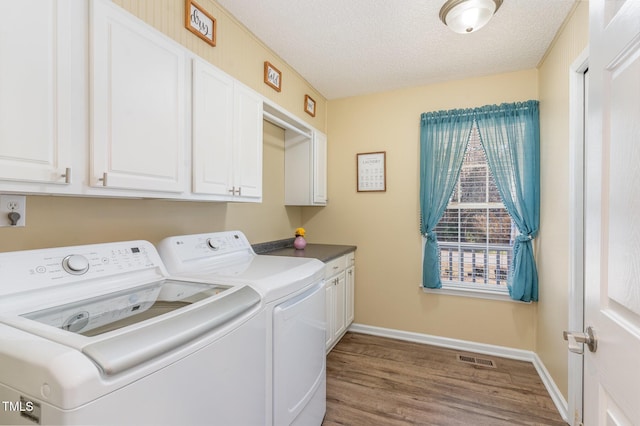 laundry area with cabinets, washing machine and clothes dryer, wood-type flooring, and a textured ceiling