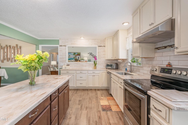 kitchen featuring sink, light hardwood / wood-style flooring, stainless steel appliances, tasteful backsplash, and a textured ceiling