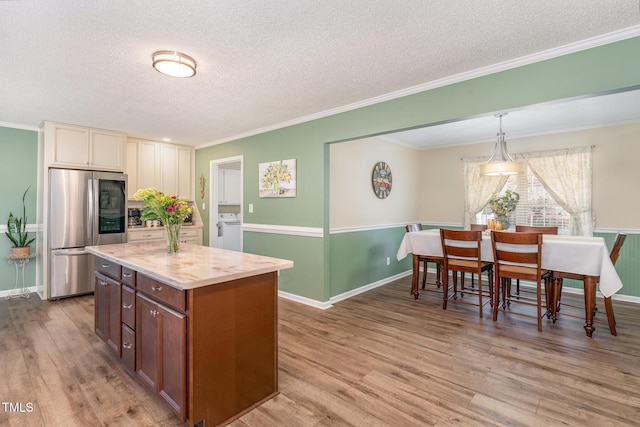 kitchen with stainless steel refrigerator, hanging light fixtures, a center island, cream cabinets, and washer / clothes dryer