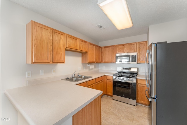 kitchen with appliances with stainless steel finishes, sink, a textured ceiling, and kitchen peninsula