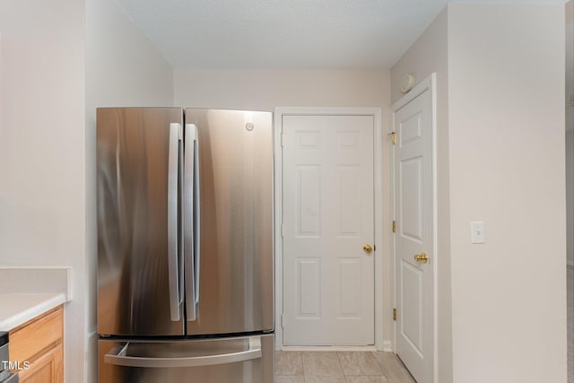 kitchen featuring stainless steel refrigerator, a textured ceiling, and light brown cabinets