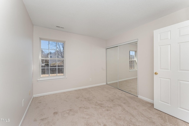 unfurnished bedroom featuring multiple windows, light colored carpet, a textured ceiling, and a closet