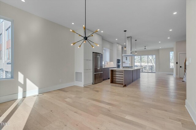 kitchen with island range hood, light wood-type flooring, high quality fridge, a kitchen island, and pendant lighting