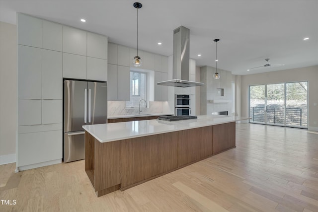 kitchen with a spacious island, white cabinetry, island range hood, hanging light fixtures, and appliances with stainless steel finishes