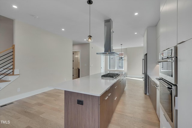 kitchen featuring pendant lighting, white cabinets, island exhaust hood, light wood-type flooring, and a spacious island