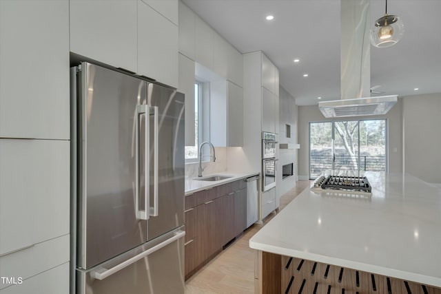 kitchen featuring sink, white cabinetry, decorative light fixtures, stainless steel appliances, and light hardwood / wood-style floors