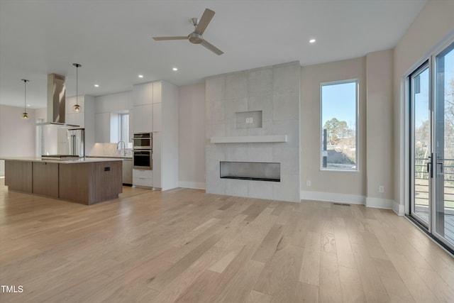 unfurnished living room with ceiling fan, a tiled fireplace, sink, and light wood-type flooring