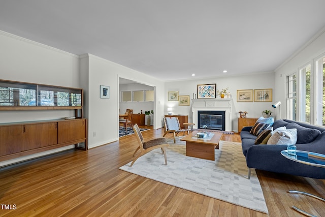 living area with wood finished floors, baseboards, recessed lighting, a glass covered fireplace, and crown molding