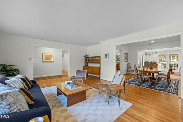 living area with a chandelier, baseboards, crown molding, and light wood-style floors