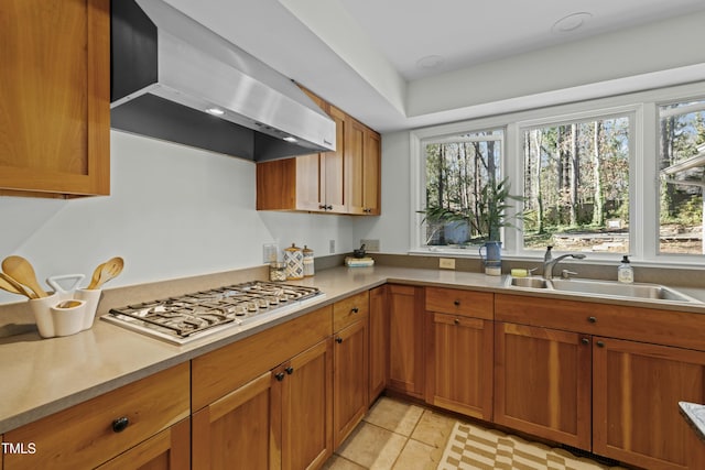 kitchen featuring stainless steel gas cooktop, light countertops, brown cabinetry, wall chimney exhaust hood, and a sink