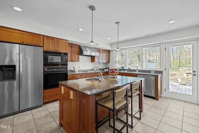 kitchen featuring dark stone counters, brown cabinetry, black appliances, wall chimney exhaust hood, and a sink