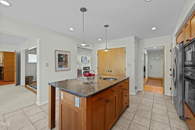 kitchen featuring a center island with sink, dark stone countertops, a kitchen breakfast bar, black appliances, and a sink