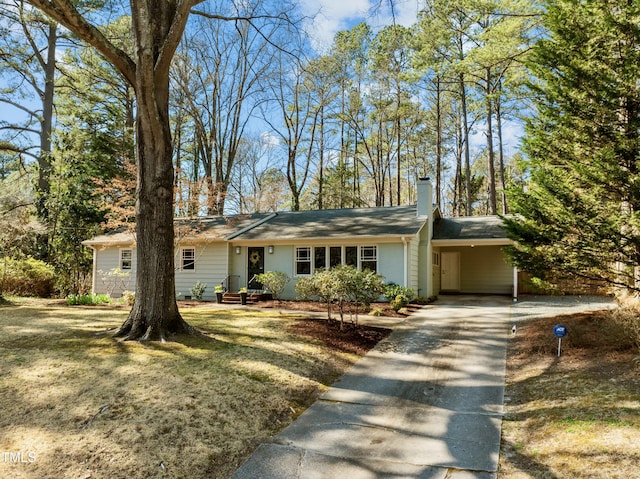 single story home with a front yard, an attached carport, concrete driveway, and a chimney