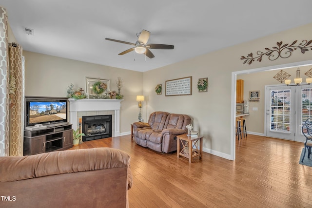 living room with a tiled fireplace, ceiling fan, and light hardwood / wood-style floors