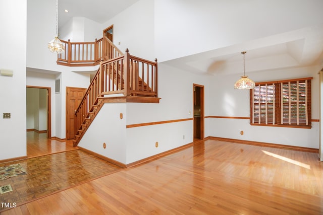 unfurnished living room featuring parquet flooring, a towering ceiling, a raised ceiling, and an inviting chandelier