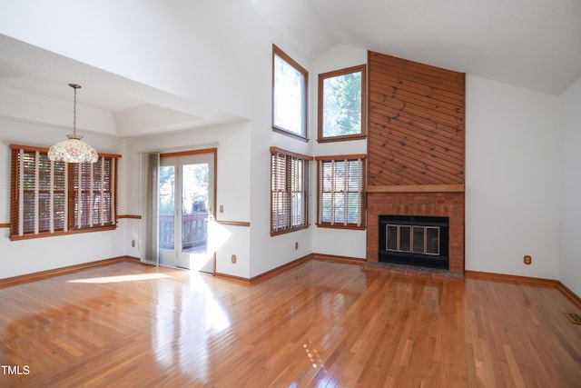 unfurnished living room featuring an inviting chandelier, a brick fireplace, wood-type flooring, and high vaulted ceiling