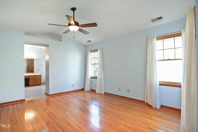 unfurnished bedroom with ceiling fan, lofted ceiling, connected bathroom, and light wood-type flooring