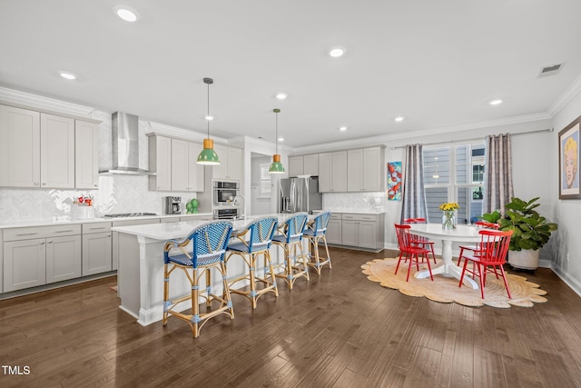 kitchen featuring appliances with stainless steel finishes, a breakfast bar area, wall chimney range hood, pendant lighting, and a spacious island