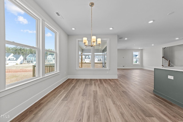 unfurnished dining area with a healthy amount of sunlight, wood-type flooring, and a notable chandelier