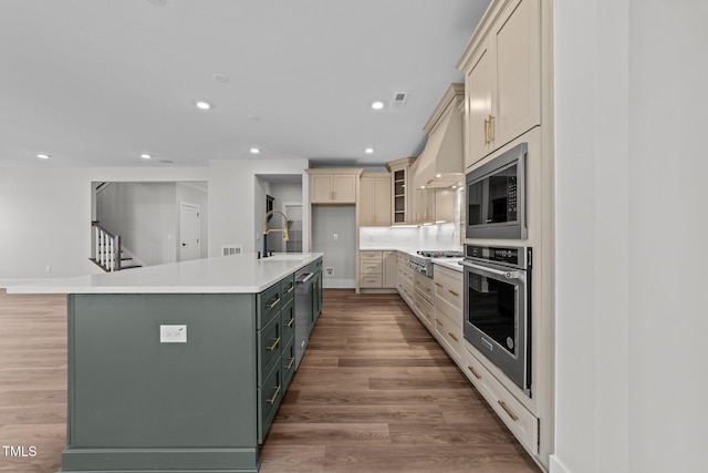 kitchen featuring tasteful backsplash, wood-type flooring, sink, stainless steel appliances, and a center island with sink