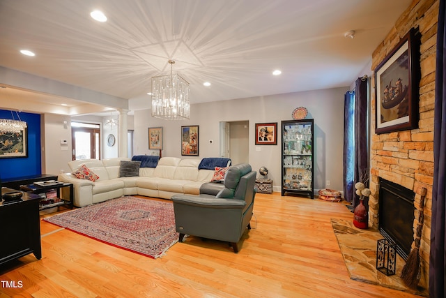 living room with ornate columns, a stone fireplace, a chandelier, and light hardwood / wood-style floors