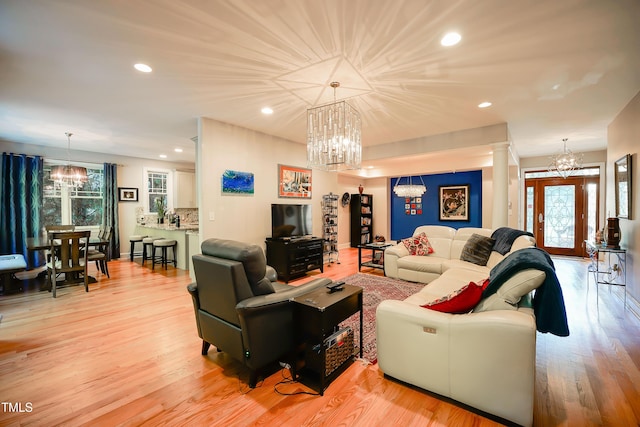 living room featuring an inviting chandelier, light hardwood / wood-style floors, and decorative columns