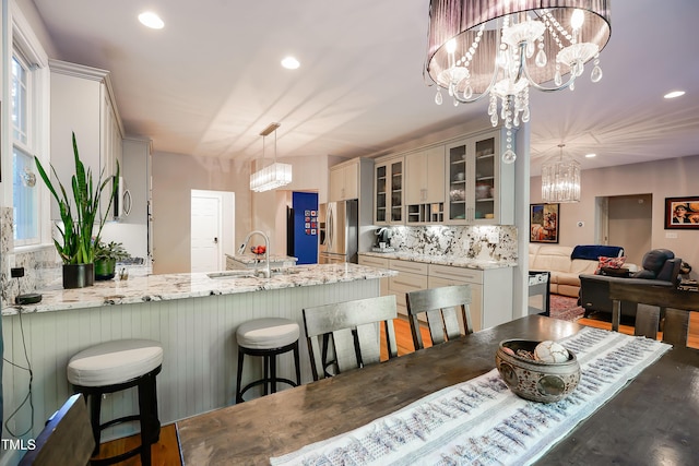 kitchen with stainless steel refrigerator with ice dispenser, sink, a chandelier, hanging light fixtures, and decorative backsplash