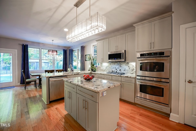 kitchen with a center island, hanging light fixtures, light wood-type flooring, kitchen peninsula, and stainless steel appliances