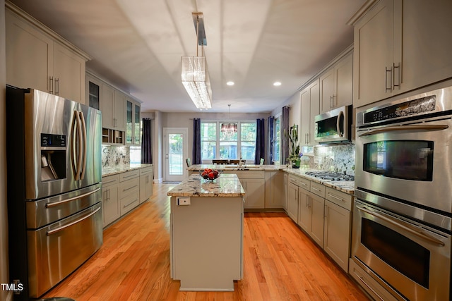 kitchen featuring gray cabinets, appliances with stainless steel finishes, light stone countertops, a kitchen island, and decorative light fixtures