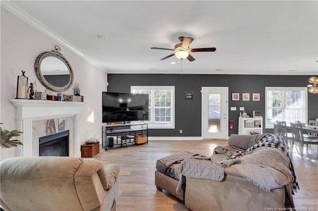 living room featuring ceiling fan, ornamental molding, a tile fireplace, and light hardwood / wood-style flooring