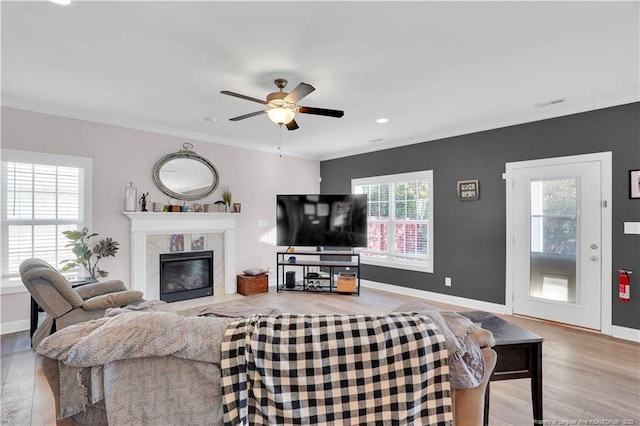 living room with ceiling fan, ornamental molding, a high end fireplace, and light hardwood / wood-style flooring