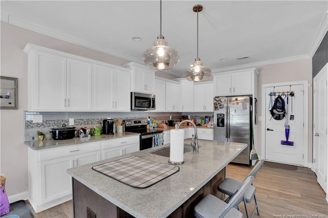 kitchen with sink, appliances with stainless steel finishes, white cabinetry, a center island with sink, and decorative light fixtures