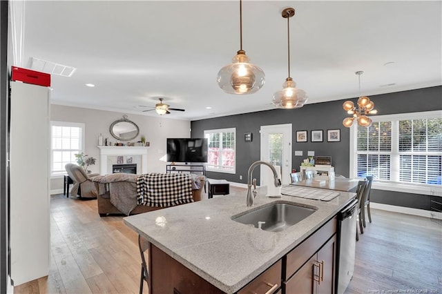 kitchen with decorative light fixtures, sink, stainless steel dishwasher, a center island with sink, and light hardwood / wood-style flooring